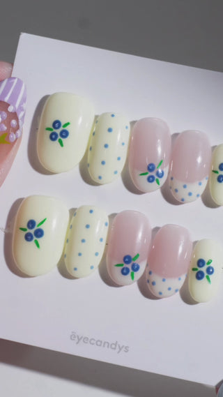 Wearing EyeCandys Blueberry Tart Press-On Nails — cream and blush base with hand-painted blueberry clusters, green leaves, and blue polka dots, short round shape