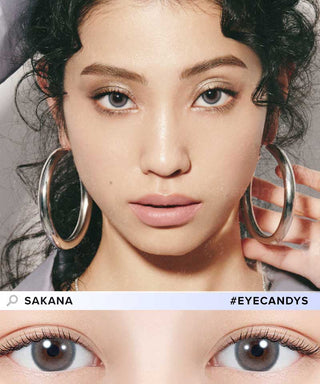 A close-up of a woman with wavy dark hair, large silver hoops, and light brown eyes wearing N's Collection Sakana Grey (10pk) contacts. Below is an eye detail shot. Text reads "N's Collection" and "#EYECANDYS". For myopia prescription.