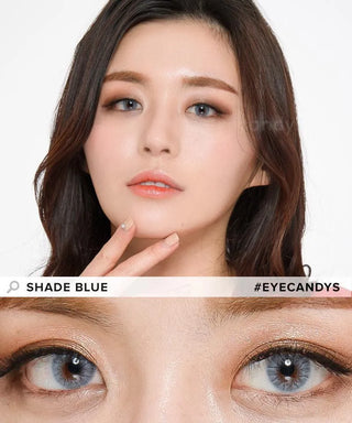 A woman with long dark hair wears EyeCandys Shade Blue contacts and natural makeup, touching her face as a close-up shows her vivid blue eyes. Text reads “SHADE BLUE” and “#EYECANDYS.”.