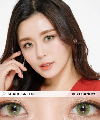 A woman with long brown hair and natural makeup touches her face, showing off EyeCandys Shade Green colored contacts. A close-up highlights the green lens for dark eyes. Text reads “SHADE GREEN” and “#EYECANDYS.”.