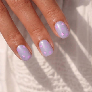 Close up hand showcasing EyeCandys Stardust Baby press on nails with lilac jelly base, pink stars, and confetti nail art.
