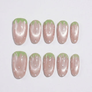Short oval press on nails EyeCandys Strawbelina with pink shimmer base, white dot details, and green tip accents inspired by strawberries.