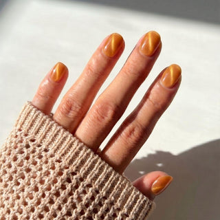 Stylish hand wearing EyeCandys Sun Drops Press-On Nails featuring bronze copper shimmer nails, glowing sunlit aesthetic.