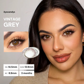 A woman with long dark hair and flawless makeup wears EyeCandys Pink Label Vintage Grey contacts. Close-up shows her dolly look, lens details (DIA 14.5mm/13.9mm, B.C. 8.9mm, 3-month use), and the lens image.