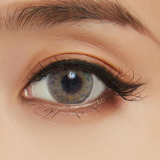 A close-up of a person's eye wearing NEO Vision Cosmo Green circle lenses by NEO Vision, with long eyelashes, a neatly groomed eyebrow, and subtle eyelid makeup.
